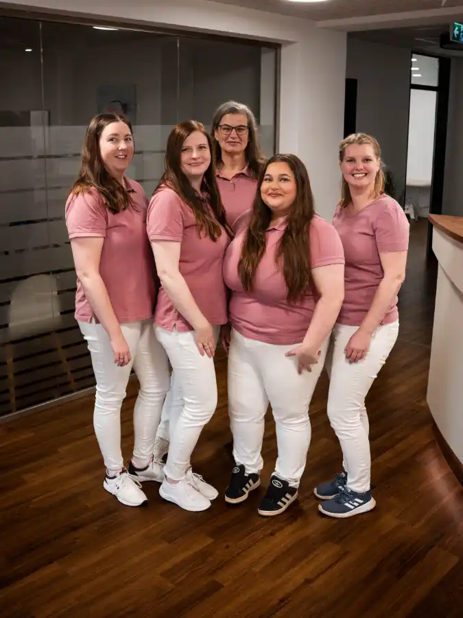 Mitarbeiterinnen der Arztpraxis Alte Feuerwache stehen gemeinsam im Eingangsbereich der Praxis für ein Gruppenfoto