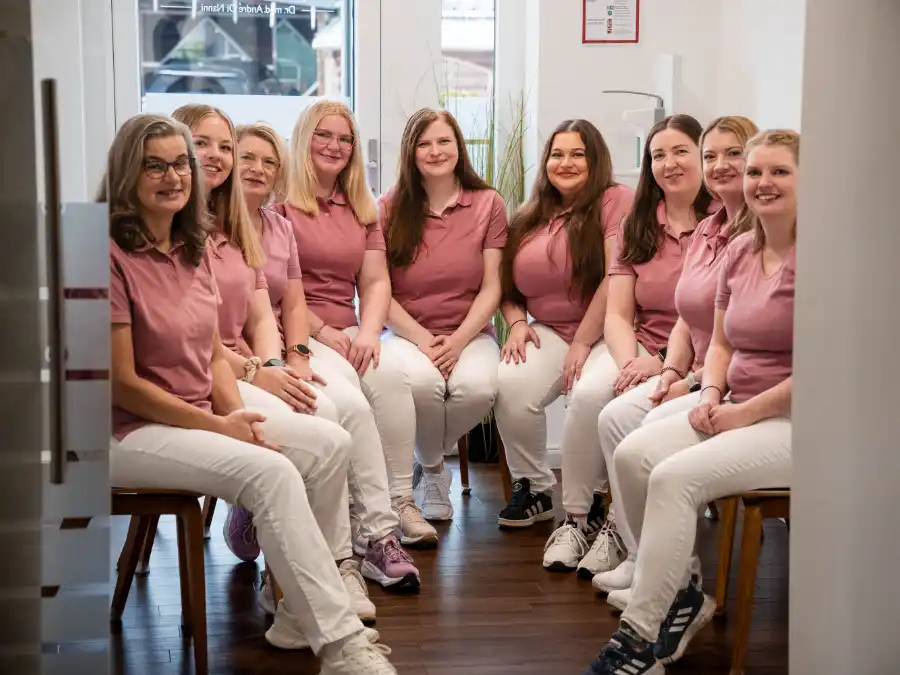 Mehrere Mitarbeiterinnen der Arztpraxis sitzen gemeinsam in einem Behandlungsraum für ein Gruppenfoto