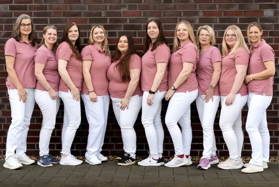 Praxisteam der Arztpraxis Alte Feuerwache steht gemeinsam vor einer Backsteinwand für ein Gruppenfoto